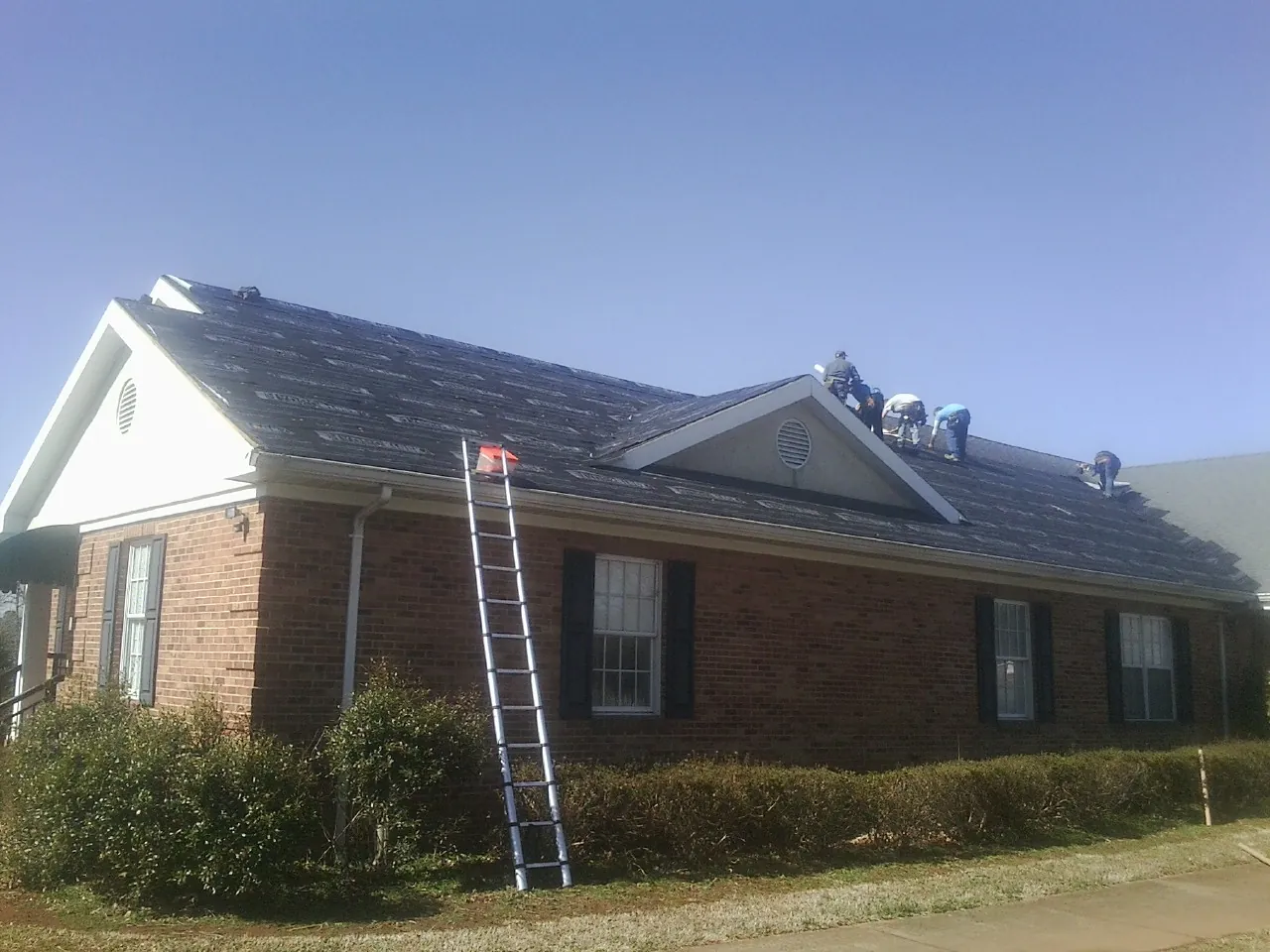 Crew tearing shingles off a brick ranch roof with a ladder set — Metal Roof Repair work by our crew in Haydenville